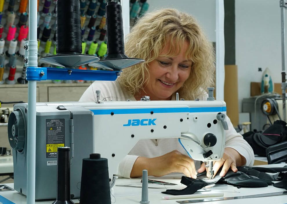 Eine Näherin bedient eine Nähmaschine und arbeitet konzentriert an Handschuhen.